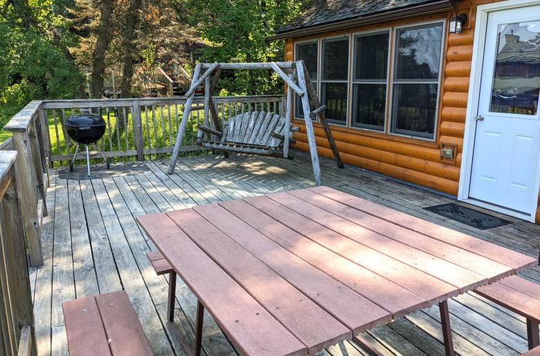 Deck area with a picnic table, charcoal grill, and swinging bench.