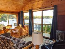Lakeside facing living room with patio doors, futon, chair, gas fireplace, and kitchen table.